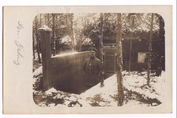 A German officer stands at the foot of a short flight of stairs leading down to a sturdy wooden cabin.
