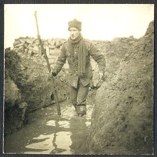 The soldier continues wading along the water-filled trench.